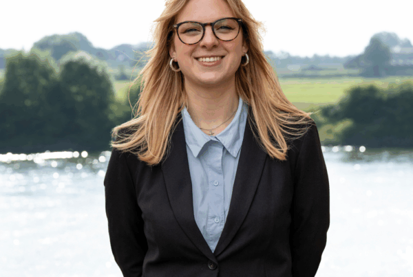 Emma Dijkstra, junior adviseur poseert in pak met water op de achtergrond